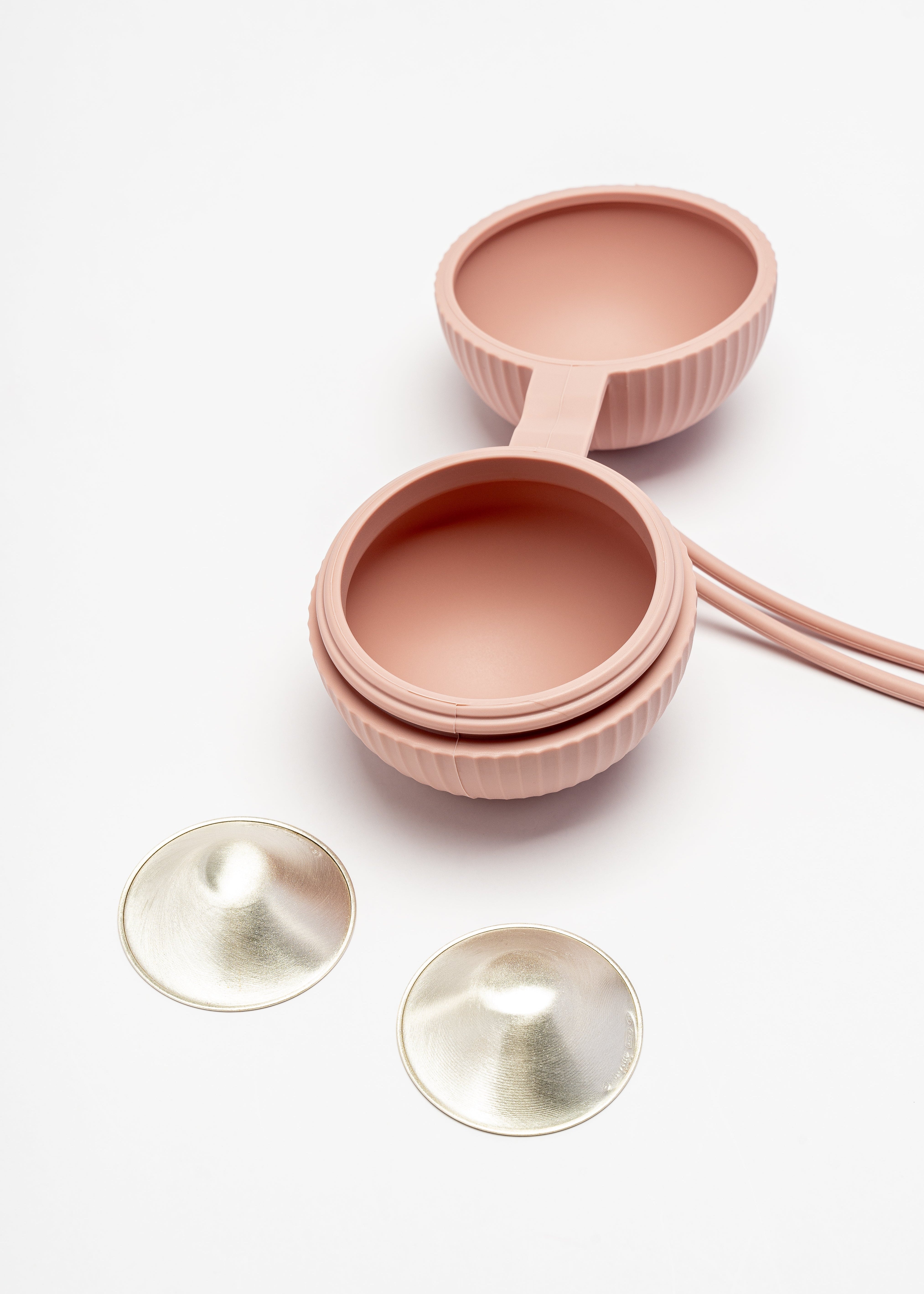 Silverette Happy Nipples pink silicone holder, open, with two Silverette silver nursing cups beside it